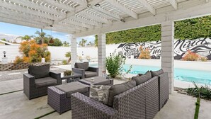 An outdoor patio with wicker furniture, a pool, and a mural on the wall.