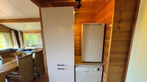 Eine kompakte Küche mit Kühlschrank, Geschirrspüler und einem Essbereich mit Korbstühlen und einem Tisch.