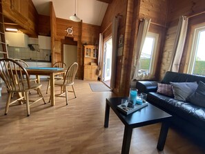 A wooden cabin interior with a dining area, kitchen, and living room. - Beachpark 2,Bungalow 62 (Renesse)