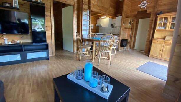Ein Holzblockhaus-Innenraum mit Essbereich, Küche und einem an der Wand befestigten Fernseher.