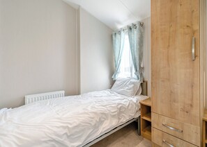 Ein Schlafzimmer mit einem Einzelbett, einem Holzschrank, einem Heizkörper und einem Fenster mit Vorhängen.
