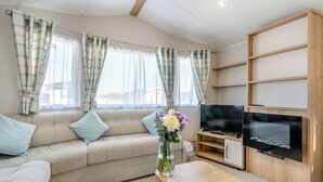 A living room with a sofa, TV, wooden shelves, and a vase with flowers. - Gold Caravan 6 WCF (Pet) (Skegness)
