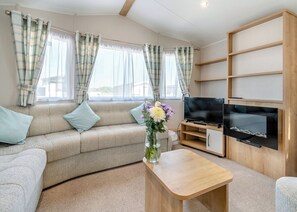 A living room with a sofa, TV, wooden shelves, and a vase with flowers.