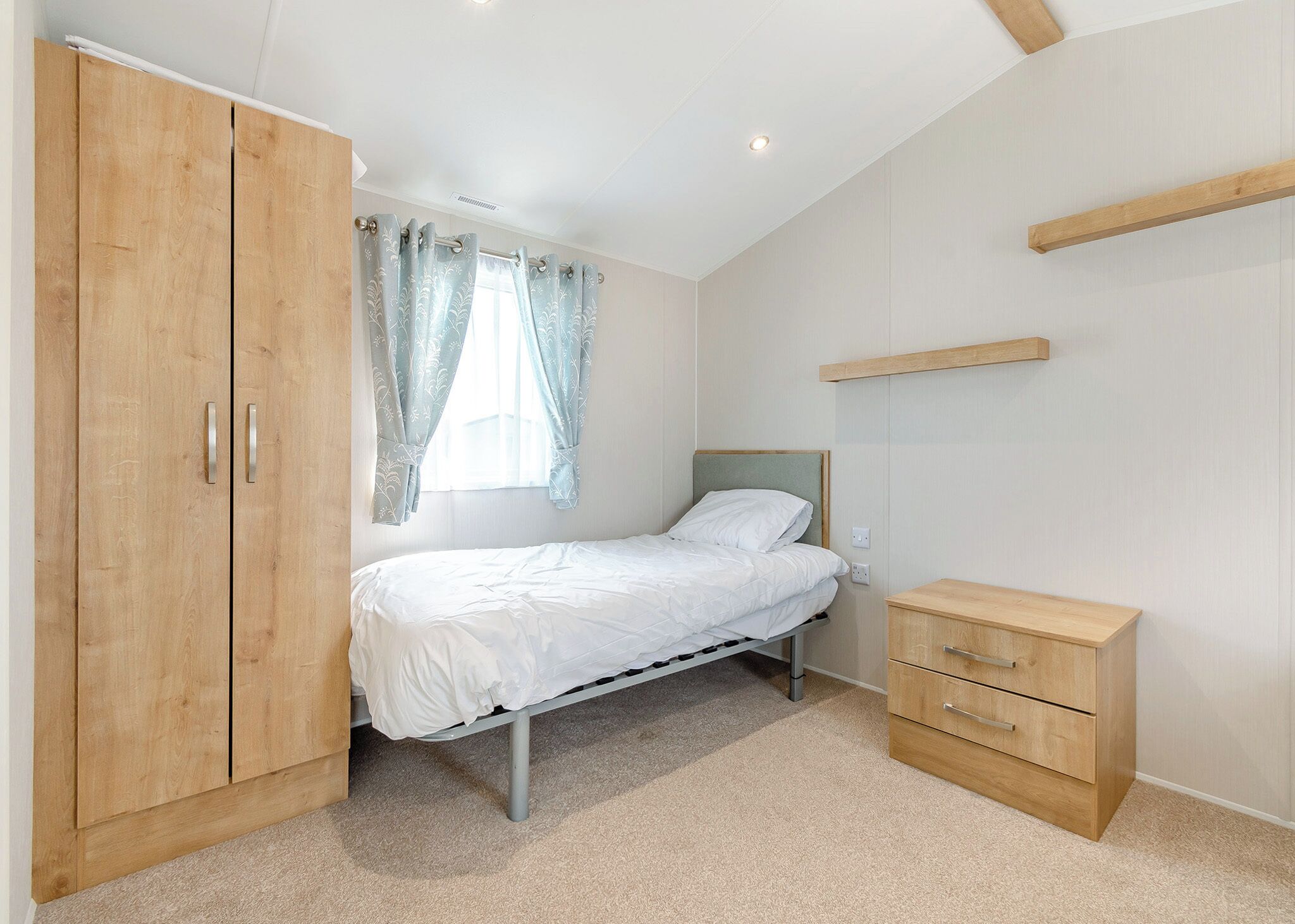 A bedroom with a bed, wooden wardrobe, and a bedside table.
