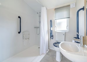 Ein Badezimmer mit Badewanne, Toilette und Waschbecken, ausgestattet mit Haltegriffen und einer Duschvorhang.