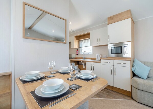 A modern kitchen with white cabinets, a microwave, and a dining table set with plates and glasses.