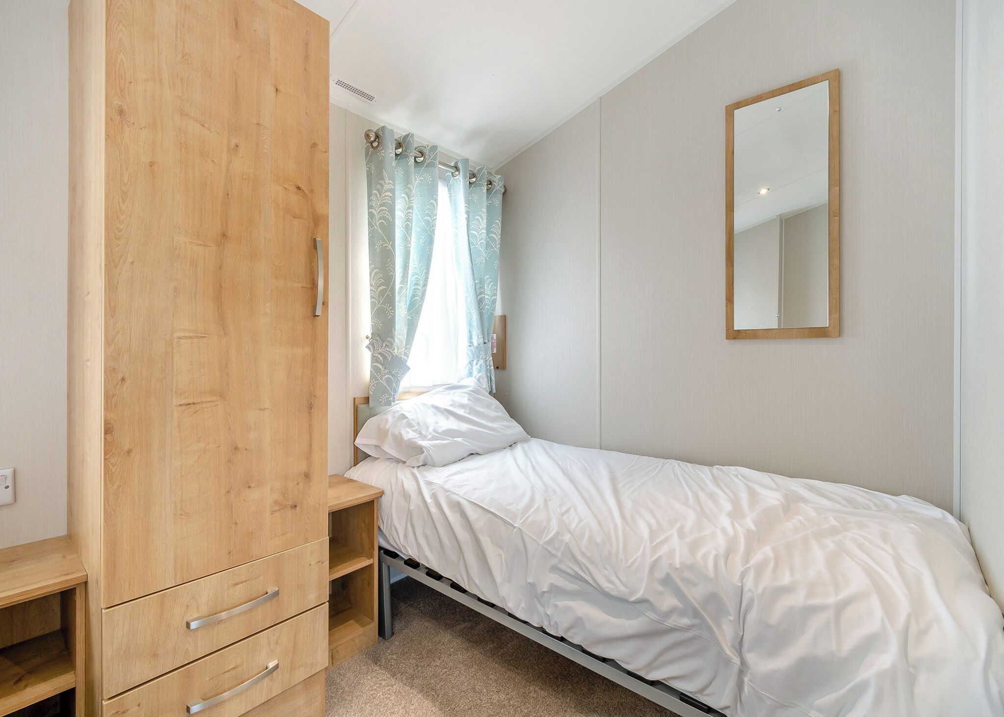 A bedroom with a bed, wooden wardrobe, and a mirror.