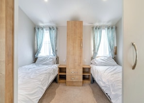 Une chambre avec deux lits simples, une commode en bois placée au centre et des rideaux bleu clair.