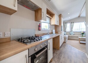 A modern kitchen with a gas stove, oven, and sink, wooden cabinets, and a window with curtains.