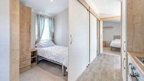A bedroom with a bed, a wardrobe, a small desk, and a bathroom visible through an open door. - Gold Caravan 6 WCF (Pet) (Skegness)