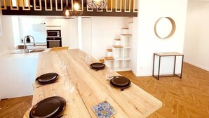 Une cuisine moderne avec un îlot central en bois, des luminaires suspendus et un escalier doté d’étagères blanches.
