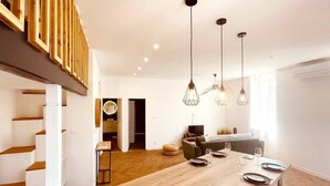 Une cuisine moderne avec une table à manger en bois, des luminaires suspendus et un escalier.