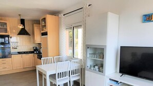 Une cuisine moderne avec des meubles en bois, une table à manger avec des chaises, un téléviseur encastré et une fenêtre avec des rideaux.