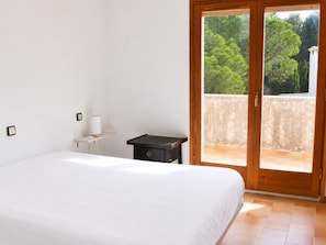 Une chambre avec un grand lit, une petite table de chevet, une lampe et une porte-fenêtre coulissante donnant sur un balcon extérieur.
