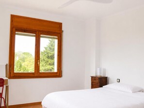 A bedroom with a large window, a bed, a nightstand, and a chair.