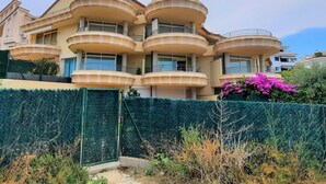 Un immeuble à plusieurs étages, doté de balcons incurvés et d’une haie verdoyante au premier plan.