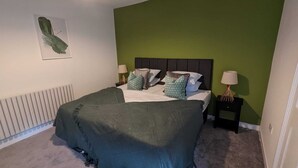 Une chambre à coucher avec un lit, des murs verts, un radiateur et un tableau encadré accroché au mur.