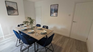 Un coin repas avec une table en bois dressée pour quatre personnes, des chaises bleues et deux tableaux encadrés accrochés aux murs.
