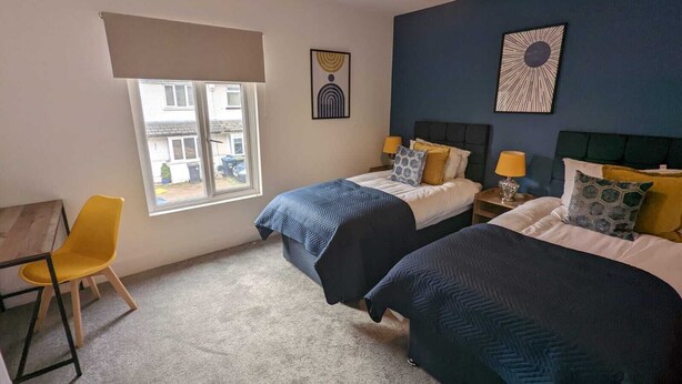 Une chambre avec deux lits, un bureau et une chaise. Il y a une fenêtre donnant sur les bâtiments environnants.