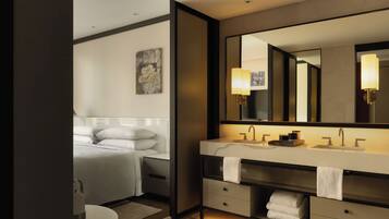 Un baño moderno con un espejo grande, tocador con lavamanos y una cama con almohadas.