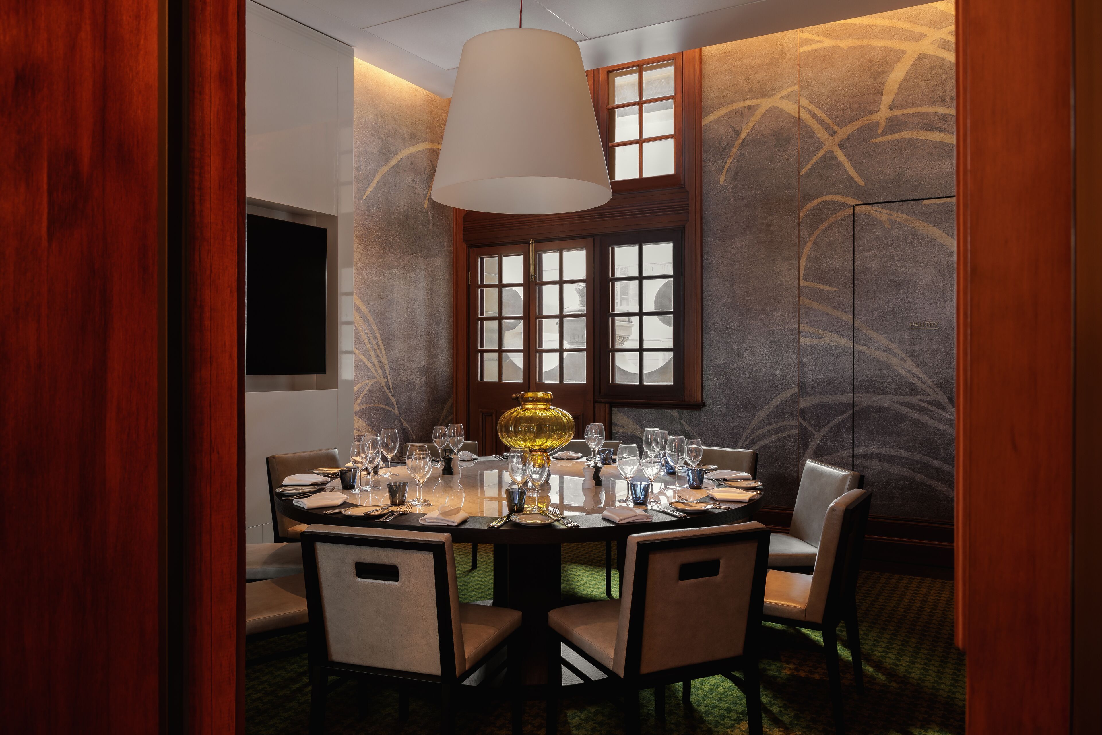 Un comedor con una mesa redonda dispuesta para seis personas, rodeada de seis sillas. Una lámpara colgante grande y blanca ilumina la mesa.