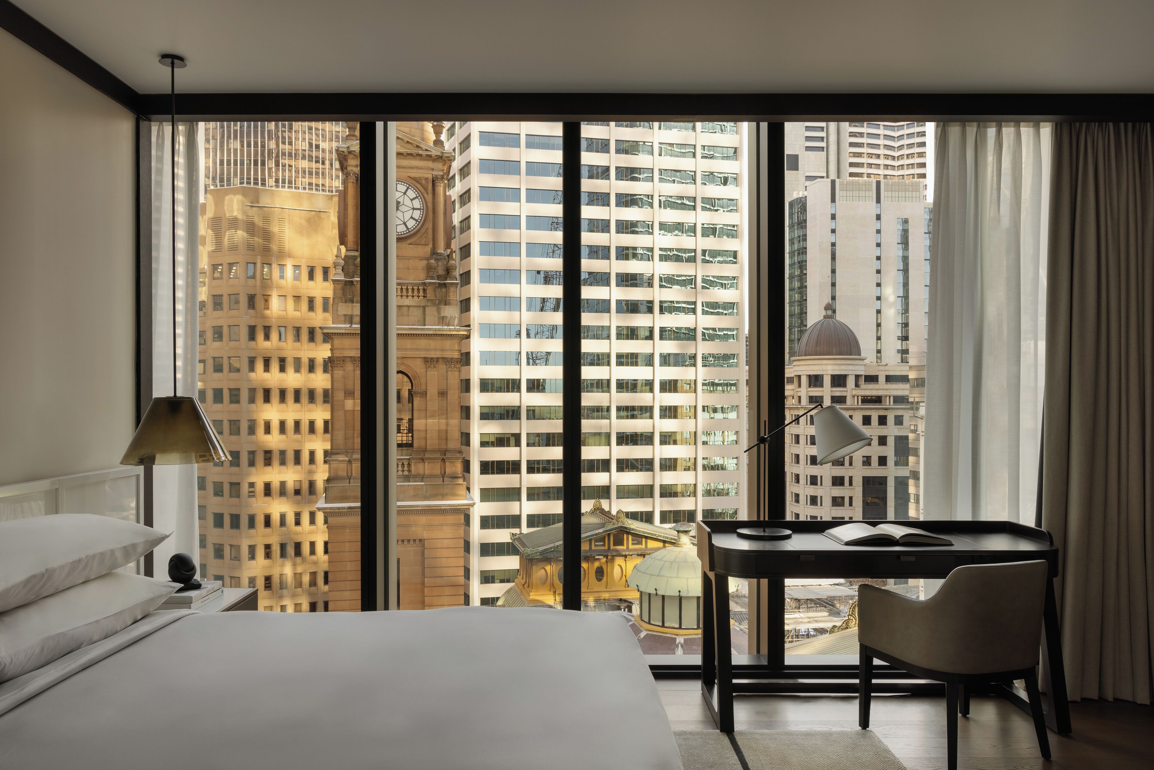 A hotel room with a large window, a bed, a desk, and a chair.