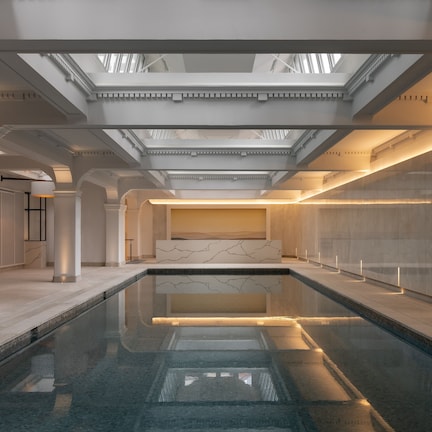 A modern indoor swimming pool with a skylight ceiling, marble walls, and a minimalist design.