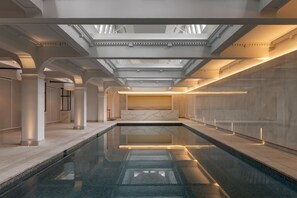A modern indoor swimming pool with a skylight ceiling, marble walls, and a minimalist design. - Capella Sydney (Sydney)