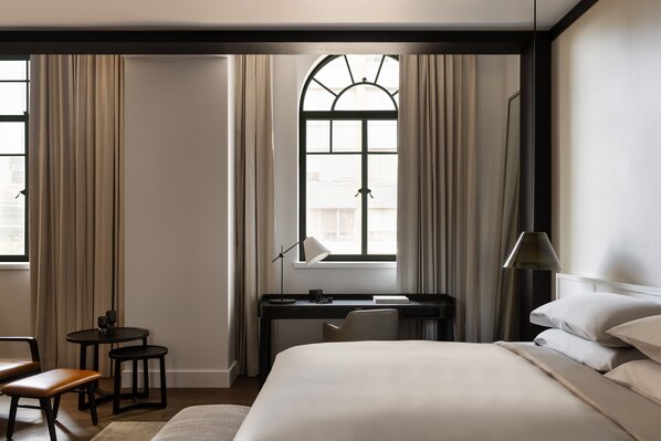 A hotel room with a bed, desk, chair, and a window with curtains. - Capella Sydney (Sydney)