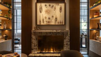 A modern living room with a fireplace, a large abstract painting, and a view through large windows.