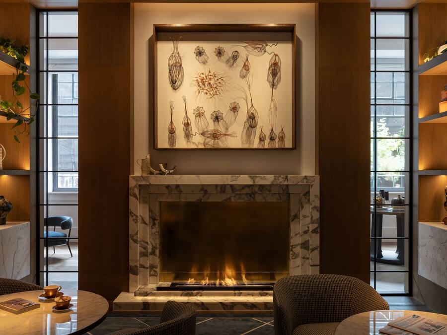 A modern living room with a fireplace, a large abstract painting, and a view through large windows.