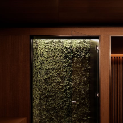 A modern bathroom with a glass door, a wooden bench, and a moss wall.