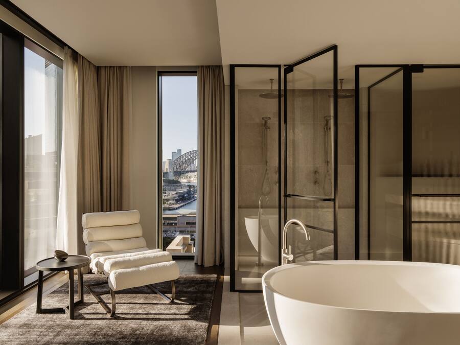 A modern bathroom with a large bathtub, a walk-in shower, and a seating area with a view of the city.