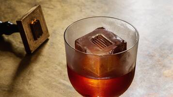 Un vaso con líquido oscuro y cubitos de hielo sobre una superficie rugosa.