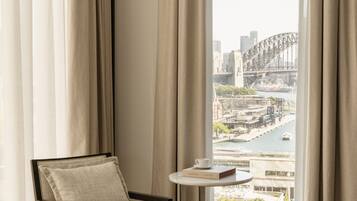 A room with a view of a bridge and cityscape, a chair, and a small table with a book.