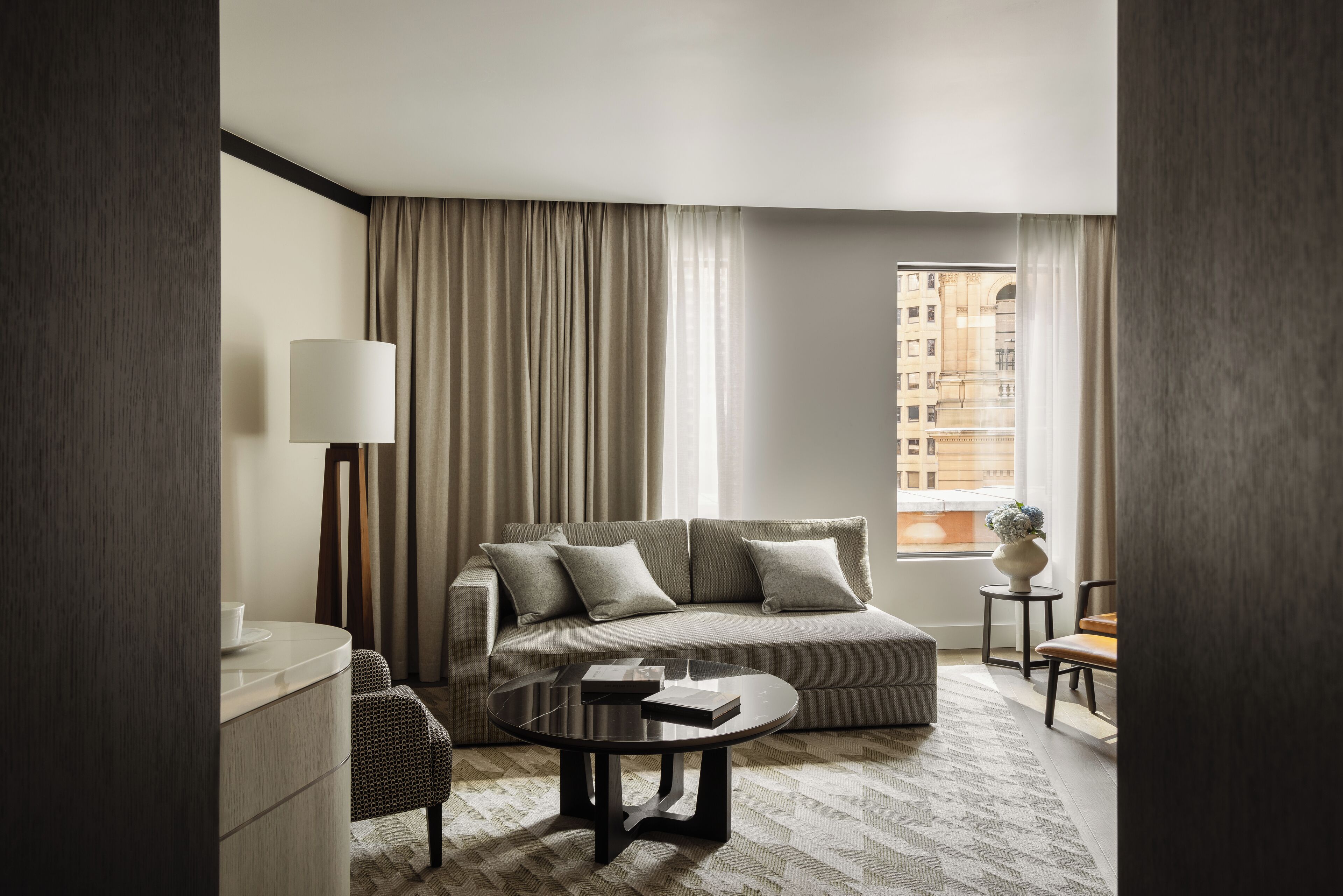 Una sala de estar moderna con un sofá, una mesa de centro, una lámpara y vistas a un edificio a través de una ventana.