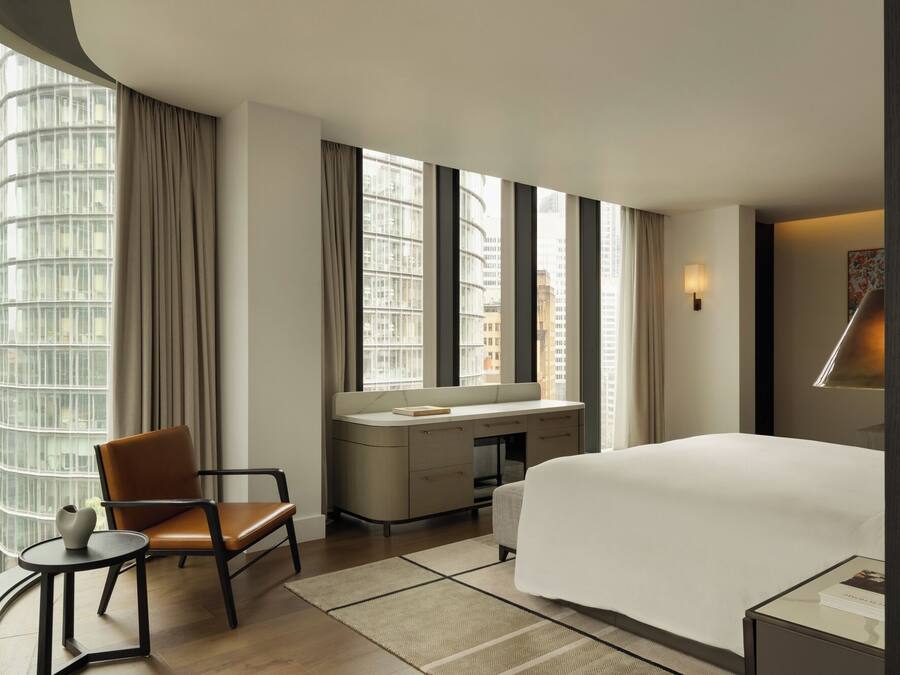A hotel room with a bed, a desk, a chair, and a large window with curtains.