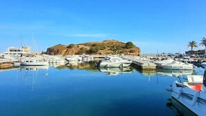 Un puerto deportivo con barcos amarrados, una colina con ruinas y cielos azules despejados.