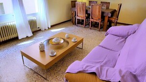 Una sala de estar con una mesa de centro de madera, un sofá morado y un comedor con sillas y mesa de madera.