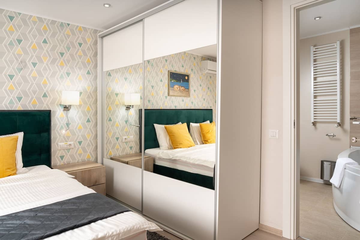 Ein Hotelzimmer mit einem Spiegelkleiderschrank, einem Bett mit weißer und gelber Bettwäsche, einem Nachttisch und einem Beistelltisch.