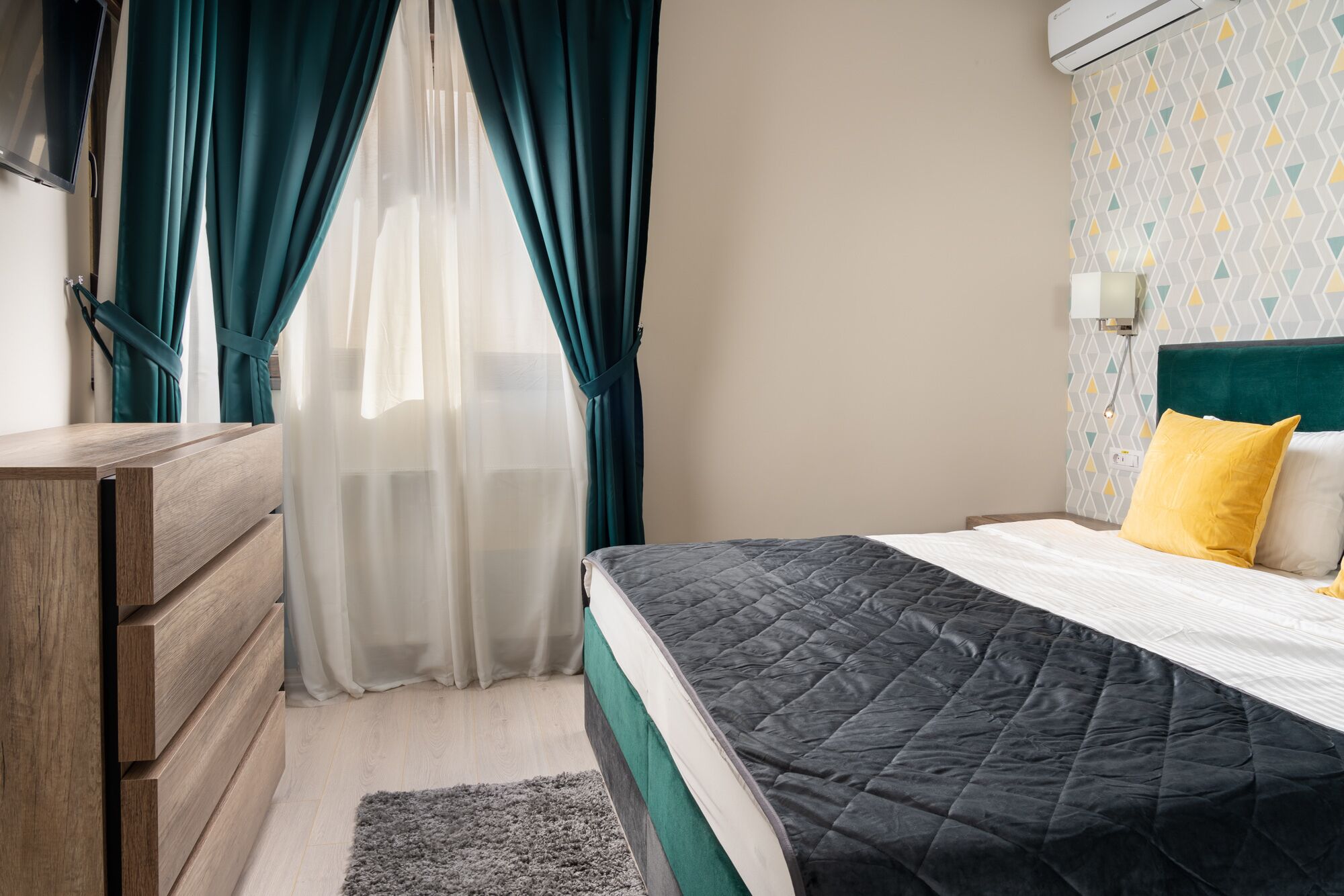 Une chambre à coucher avec un lit, une commode en bois, un bureau et une fenêtre ornée de rideaux turquoise.