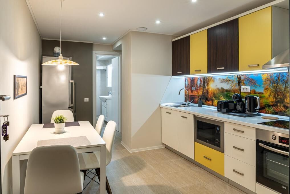 A modern kitchen with yellow and white cabinets, a dining area with a table and chairs, and a pendant light.