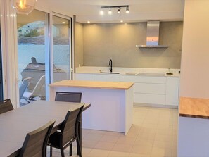 Una cocina moderna con una isla central, armarios blancos y vistas a través de un ventanal.