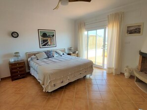 A bedroom with a bed, a nightstand, a lamp, a painting, a clock, and a fireplace.
