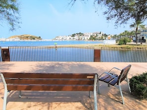 A bench and chair by a waterfront with a view of buildings across the water.