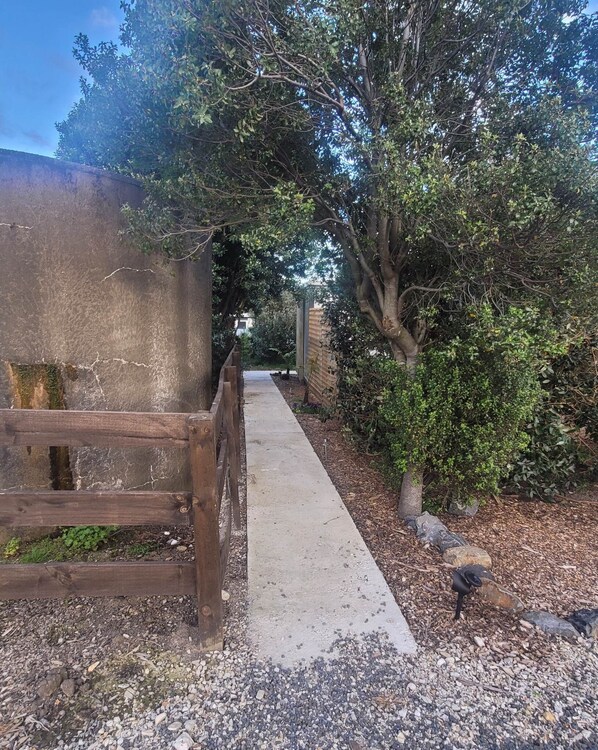 Un sendero bordeado por árboles y una valla de madera que lleva a un edificio con un muro de piedra.