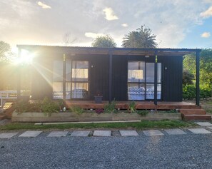 Una casa moderna con puerta y ventanas de vidrio, rodeada por un jardín con terraza de madera y camino de grava.