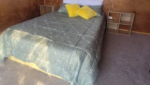 Makuuhuoneessa on sänky, kaksi ikkunaa, joissa on pitsiverhot, puinen pääty ja pieni puinen yöpöytä.