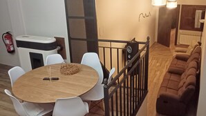 A dining area with a round wooden table and white chairs, a black metal railing, and a brown sofa in the background. - RURAL HOUSE THE VIEWPOINT OF SAN MIGUEL (San Esteban de Gormaz)