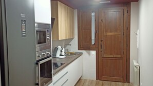 A compact kitchen with a refrigerator, microwave, and oven. There is a wooden door and a white radiator on the wall. - RURAL HOUSE THE VIEWPOINT OF SAN MIGUEL (San Esteban de Gormaz)